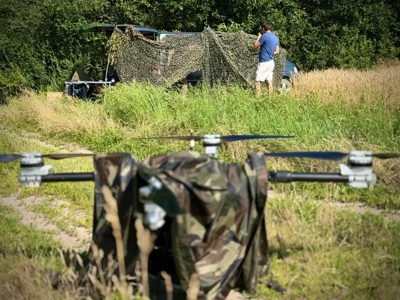 Maskuotas sunkusis multirotorius pievoje, už jo maskuojamoji palapinė