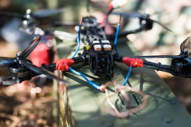 FPV drono rėmas raudona juosta apvyniotomis rankomis ant žalios šovinių dėžės, stambiu planu