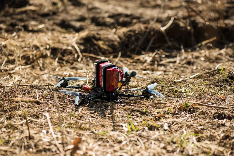 FPV dronas su raudonu kroviniu ant sausos žemės