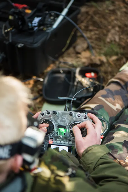 Operatorius iš nugaros laiko RadioMaster pultą po antžeminės stoties dėže