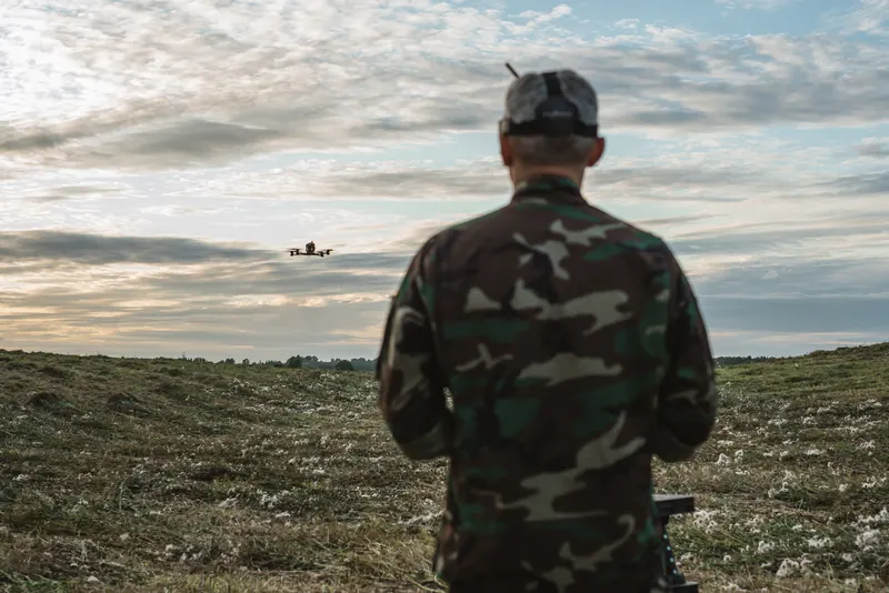 FPV pilotas iš nugaros, dronas skrenda virš lauko sutemus