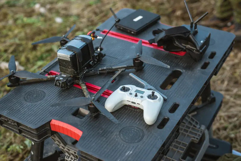 FPV dronas, baltas pultas ir akiniai ant juodo nešiojamo darbastalio