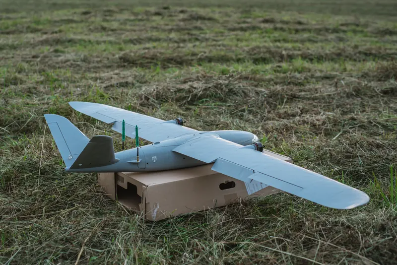 Pilkas fiksuoto sparno dronas ant kartoninės dėžės nupjautame lauke