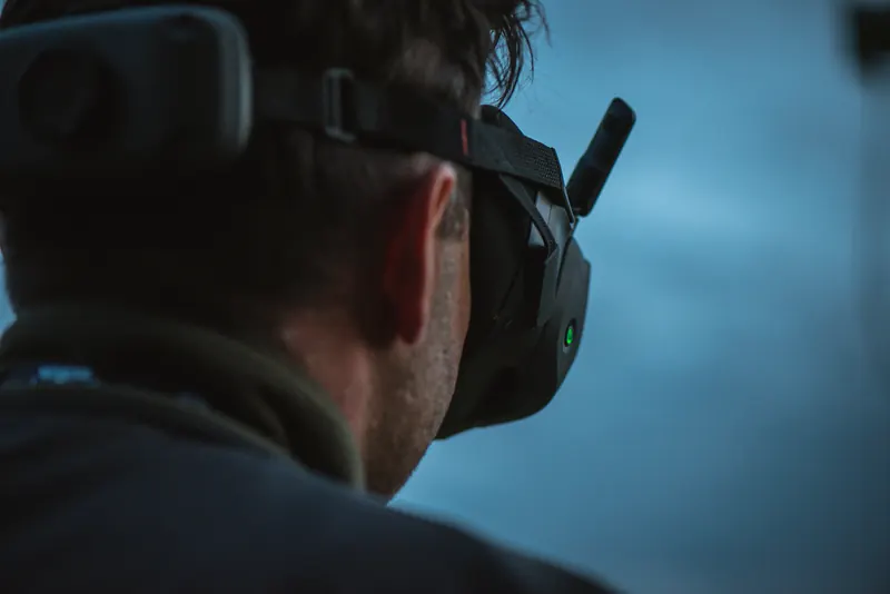 FPV pilotas su DJI akiniais iš nugaros mėlyno sutemų dangaus fone